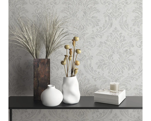 Dekoratívne zátišie s vázami, okrasnými rastlinami, sviečkou a knihou na konzole pred vzorovanou tapetou