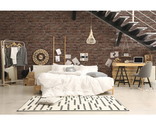 Spálňa s posteľou, stolom a schodiskom pred tehlovou stenou