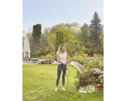 Žena zalieva kvety záhradnou hadicou v záhrade.