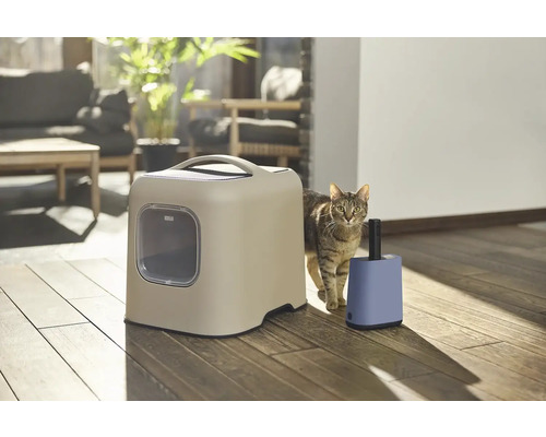 Mačka vedľa mačacej toalety a osviežovača vzduchu vo svetlej miestnosti.