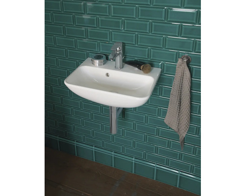 Umývadlo s vodovodnou batériou, miskou na mydlo a uterákom pred obloženou stenou