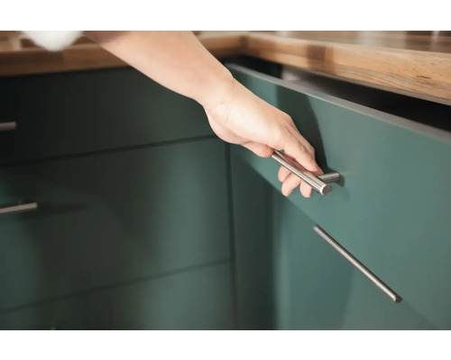 Detailný záber ruky otvárajúcej kuchynskú skrinku so striebornou úchytkou.