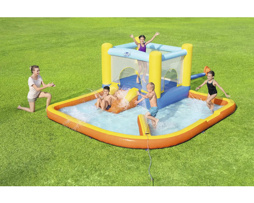 Nafukovací detský bazén so šmýkačkou a skákacím hradom na zelenom trávniku s hrajúcimi sa deťmi a ženou.