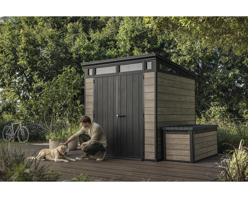 Záhradná scéna s domčekom na náradie a truhlou, muž hladí psa