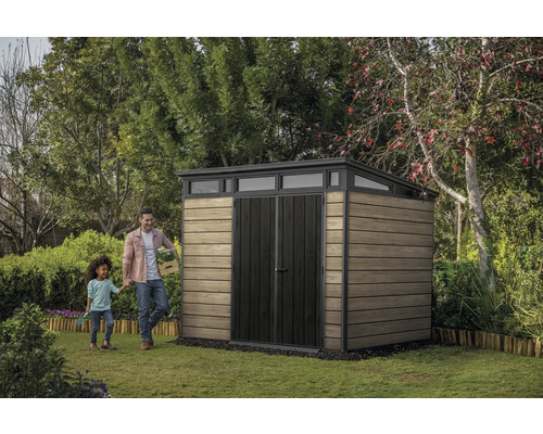 Záhradná scéna s domčekom na náradie, mužom a dieťaťom na trávniku.