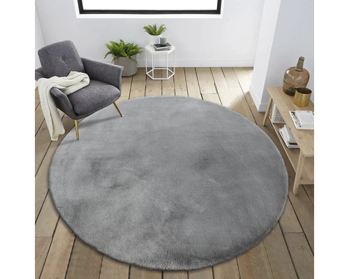 Interiérová scéna s okrúhlym sivým kobercom, kreslom a príručným stolíkom