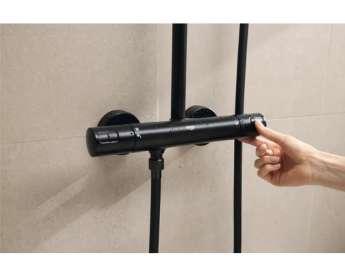 Čierny sprchový termostat ovládaný rukou pred obloženou stenou