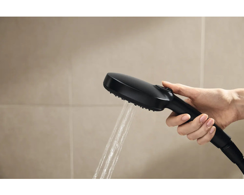 Ruka drží čiernu sprchovú hlavicu s tečúcou vodou