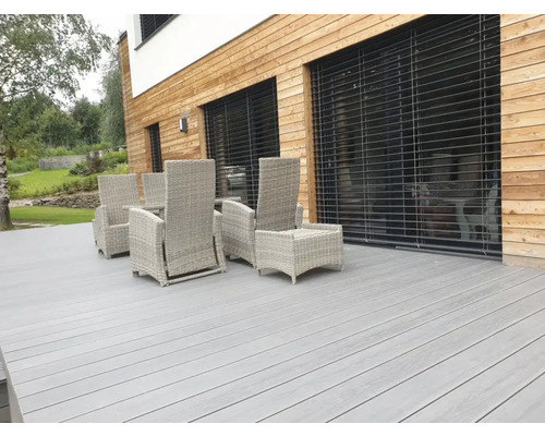 Terasa so sivou drevenou podlahou a ratanovým nábytkom pred domom s drevenou fasádou.