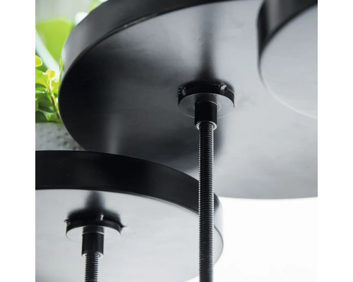 Detailný záber čierneho, viacposchodového stojana na rastliny s okrúhlymi policami a závitovými tyčami.