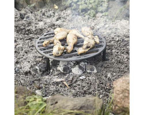 Okrúhly grilovací rošt s kuracími paličkami stojí nad táborákom.