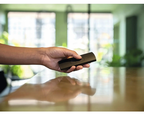 Ruka drží čierne diaľkové ovládanie.