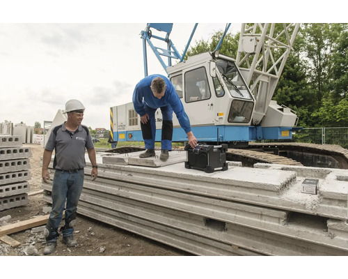 Dvaja stavební robotníci so staveniskovým rádiom a prefabrikovanými betónovými dielmi pred žeriavom
