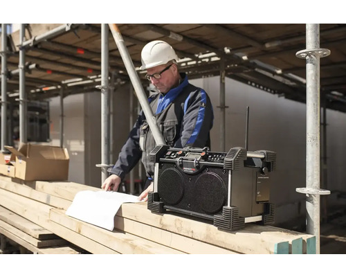 Stavebné rádio so stavebným robotníkom, ktorý sa pozerá na plány