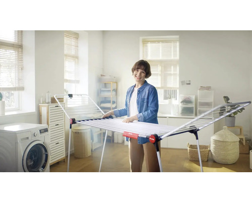 Žena vo svetlej miestnosti vedľa sušiaka na bielizeň a práčky.