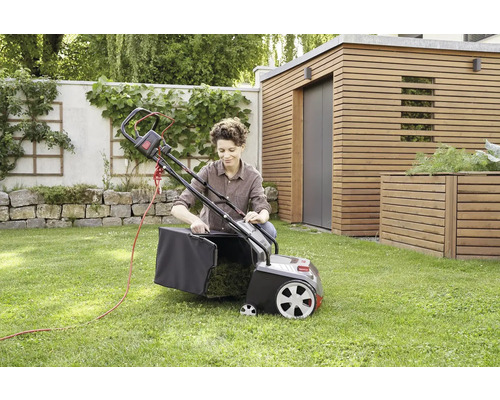 Žena pripevňuje zberný kôš k elektrickému prevzdušňovaču trávnika v záhrade.