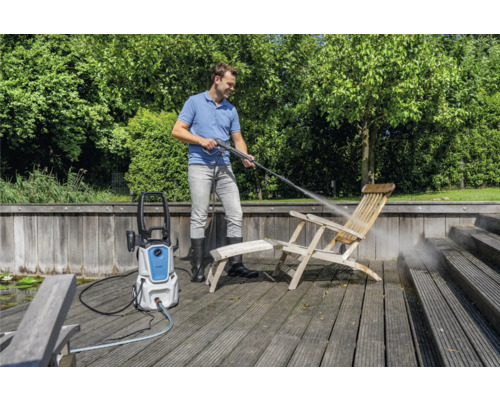 Muž čistí drevenú stoličku vysokotlakovým čističom vonku.