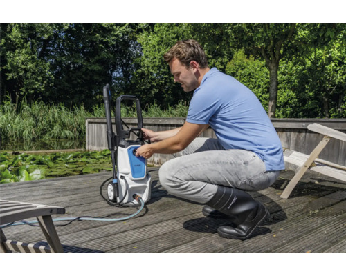 Muž obsluhuje vysokotlakový čistič vonku na drevenej terase pri vodnej ploche