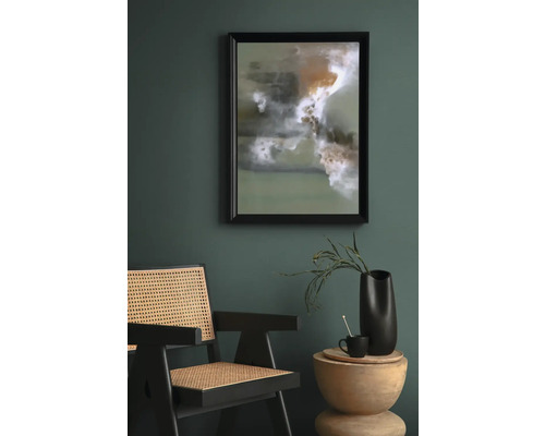 Scéna s abstraktným umeleckým dielom v ráme, ratanovým kreslom a príručným stolíkom s dekoráciou.