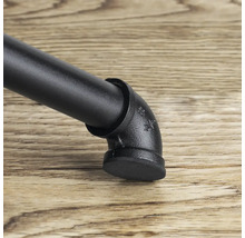 Detailný záber čiernej nohy nábytku v industriálnom dizajne s rúrkovými prvkami na drevenej podlahe.