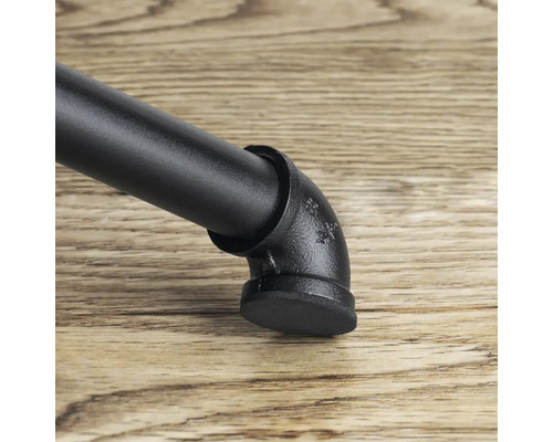 Detailný záber čiernej nohy nábytku v industriálnom dizajne s rúrkovými prvkami na drevenej podlahe.