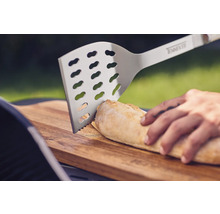 Nerezová grilovacia obracačka krája chlieb na drevenej doske.