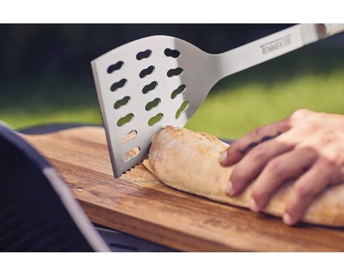 Nerezová grilovacia obracačka krája chlieb na drevenej doske.