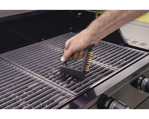 Osoba čistí grilovací rošt grilovacou kefou.