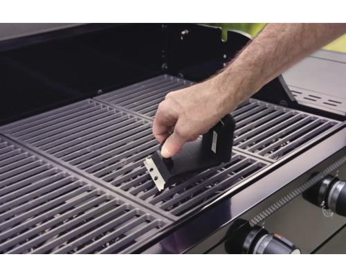 Osoba čistí grilovací rošt grilovacou kefou.