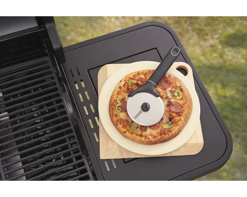 Pizza na drevenej doske s krájačom na pizzu vedľa grilu