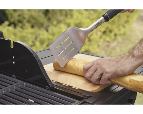 Osoba krája bagetu grilovacou obracačkou na grile.