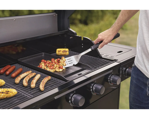 Osoba griluje klobásy, kukuricu a zeleninu na plynovom grile.