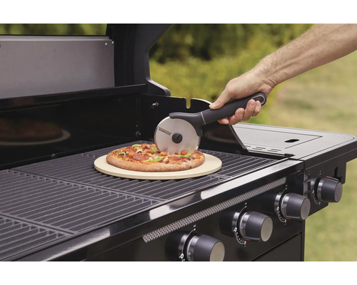 Osoba krája pizzu na grile s pizza kameňom a krájačom pizze