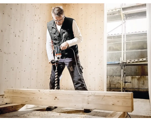 Muž vŕta drevenú dosku vŕtačkou