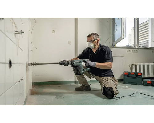 Muž vŕta dieru do obkladanej steny pomocou vŕtacieho kladiva