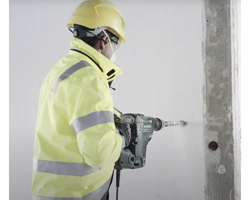 Stavebný robotník vŕta zbíjacím kladivom otvor do steny.
