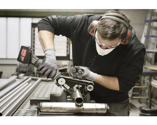 Remeselník opracováva kovovú rúrku pomocou pásovej brúsky na rúrky od spoločnosti Metabo a pritom nosí ochranné pomôcky.