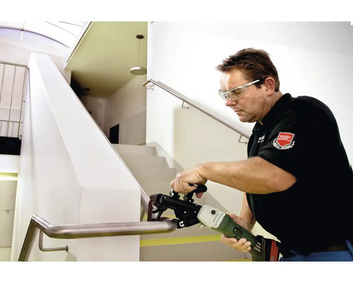 Muž brúsi zábradlie schodiska pomocou pásovej brúsky na rúrky.