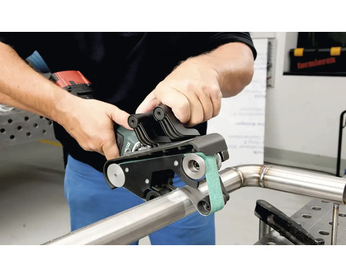 Osoba používa pásovú brúsku na rúrky na kovovej rúrke.