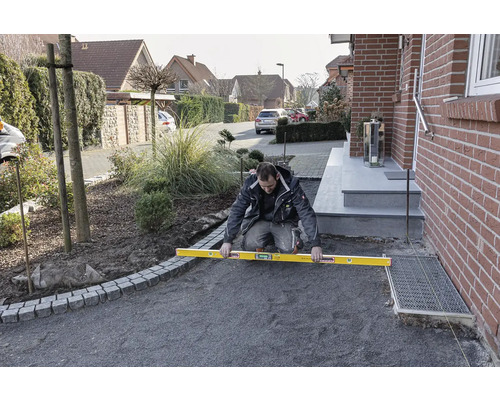 Muž používa vodováhu na vyrovnanie povrchu pre vonkajšiu dlažbu.