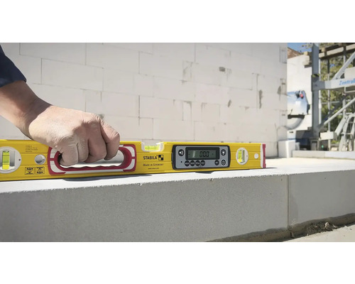 Žltá digitálna vodováha s rukou na murive