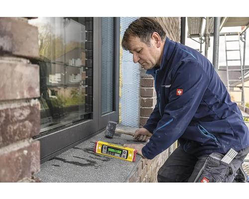 Remeselník pomocou digitálnej vodováhy vyrovnáva okenný parapet.