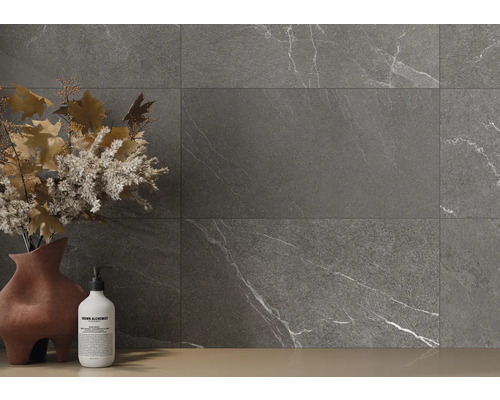 Sivé dlaždice s mramorovým vzhľadom na stene, doplnené vázou s kvetinovou výzdobou a fľaštičkou mydla