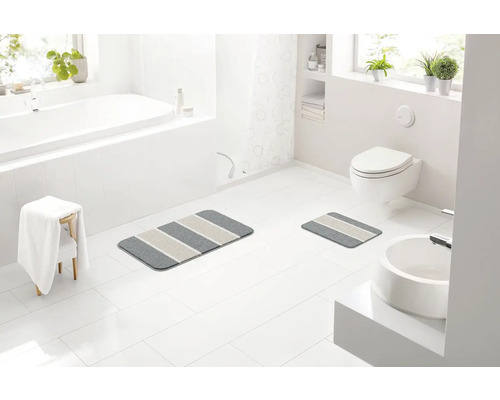 Kúpeľňa s vaňou, umývadlom, toaletou a dvoma pruhovanými kúpeľňovými predložkami.