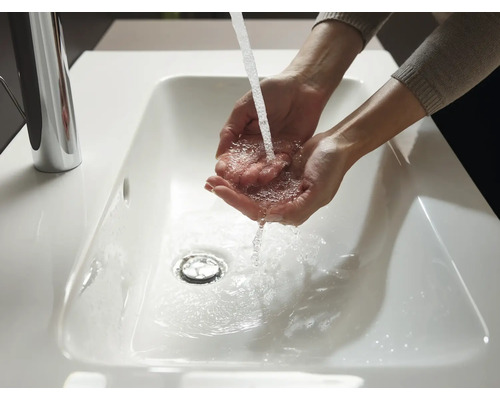 Osoba si umýva ruky v bielom umývadle s vodovodnou batériou.