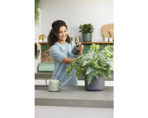 Žena sa stará o rastlinu pomocou rozprašovača vedľa kanvy na pracovnej doske