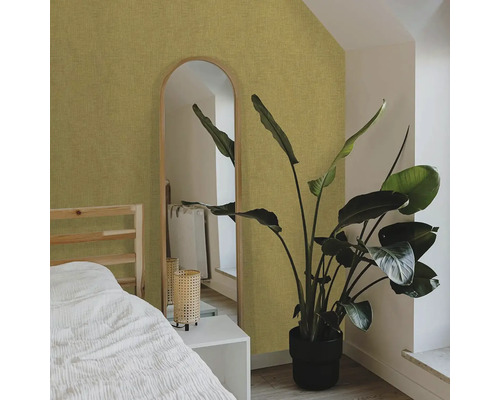 Spálňa s posteľou, zrkadlom a izbovou rastlinou pred štruktúrovanou tapetou