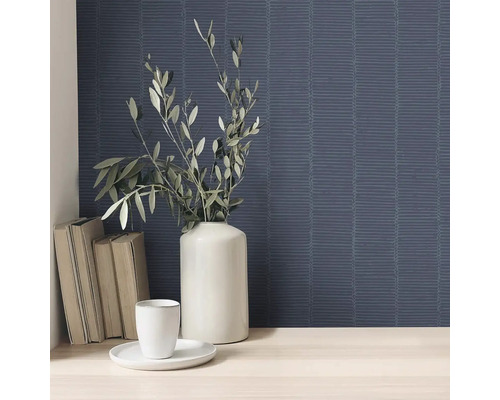 Scéna so vzorovanou tapetou, vázou s vetvami, šálkou, tanierom a knihami.