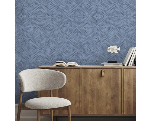 Obývacia izba s modrými vzorovanými tapetami, drevenou komodou a stoličkou.