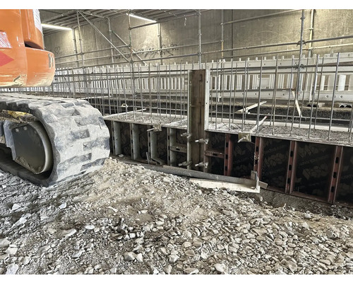 Stavebná jama s debnením a armovacím železom, pásové rýpadlo v popredí.